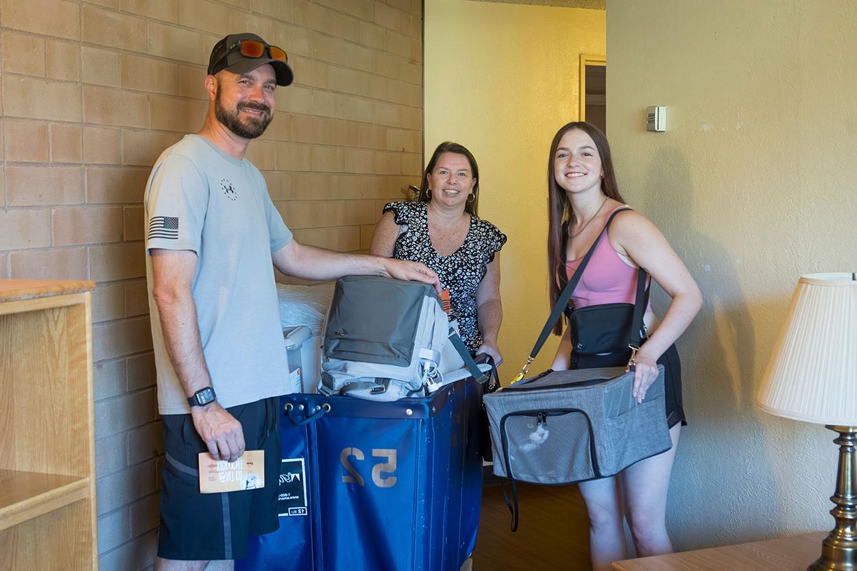 Family poses in their student's dorm room with luggage.